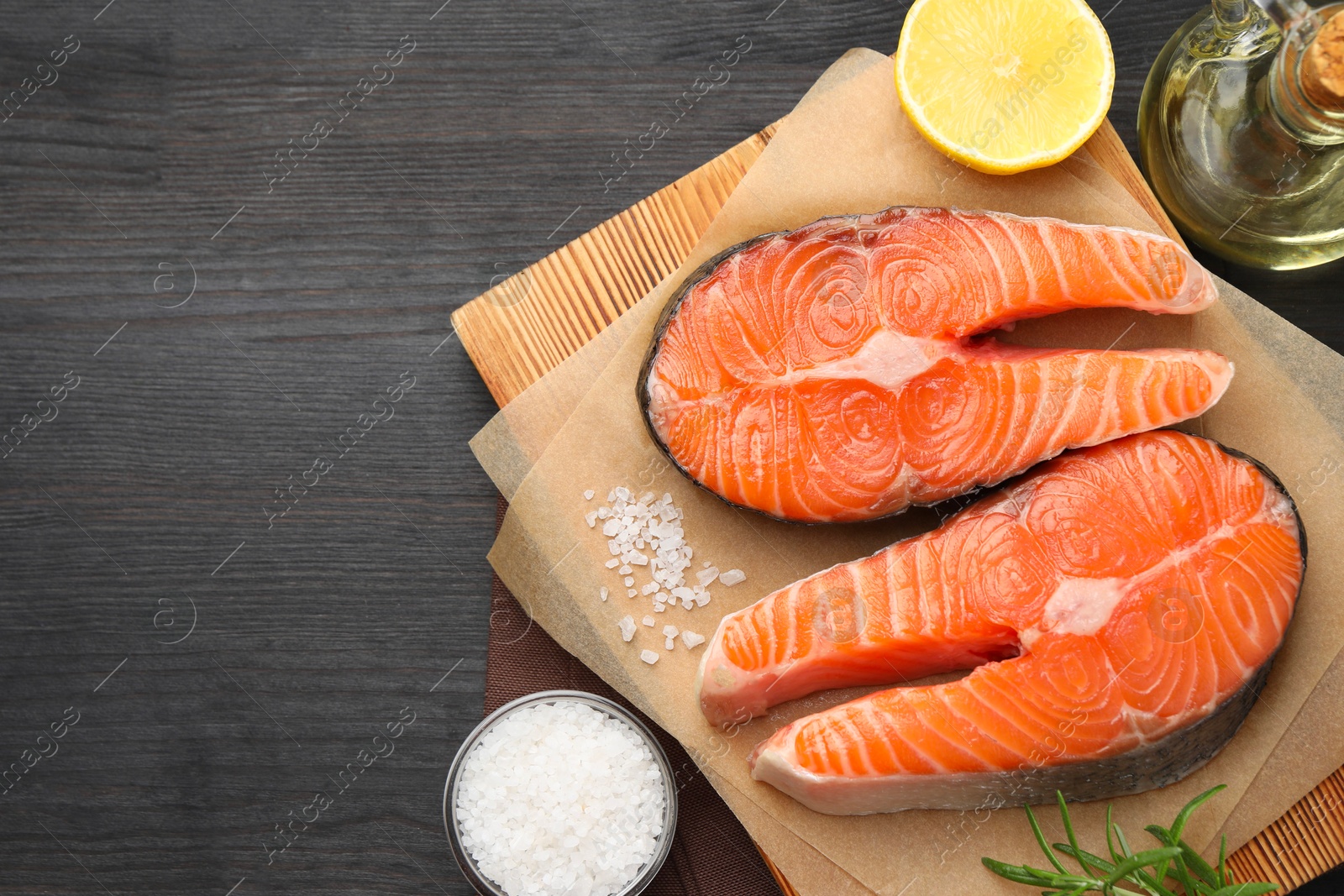 Photo of Fresh raw salmon steaks and spices on black wooden table, flat lay. Space for text