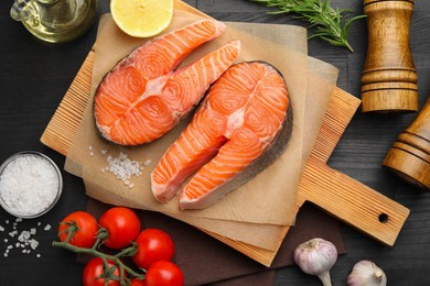 Photo of Fresh raw salmon steaks and products on black wooden table, flat lay