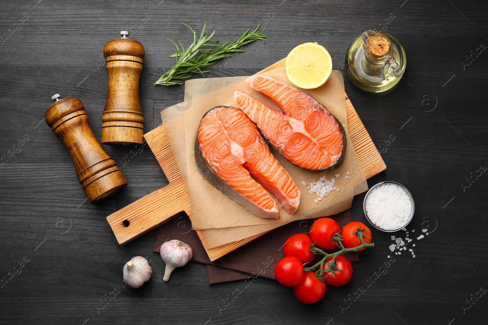 Photo of Fresh raw salmon steaks and products on black wooden table, flat lay