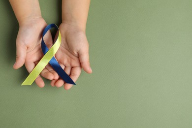 Photo of Child with yellow and blue ribbon on green background, top view. Down syndrome awareness