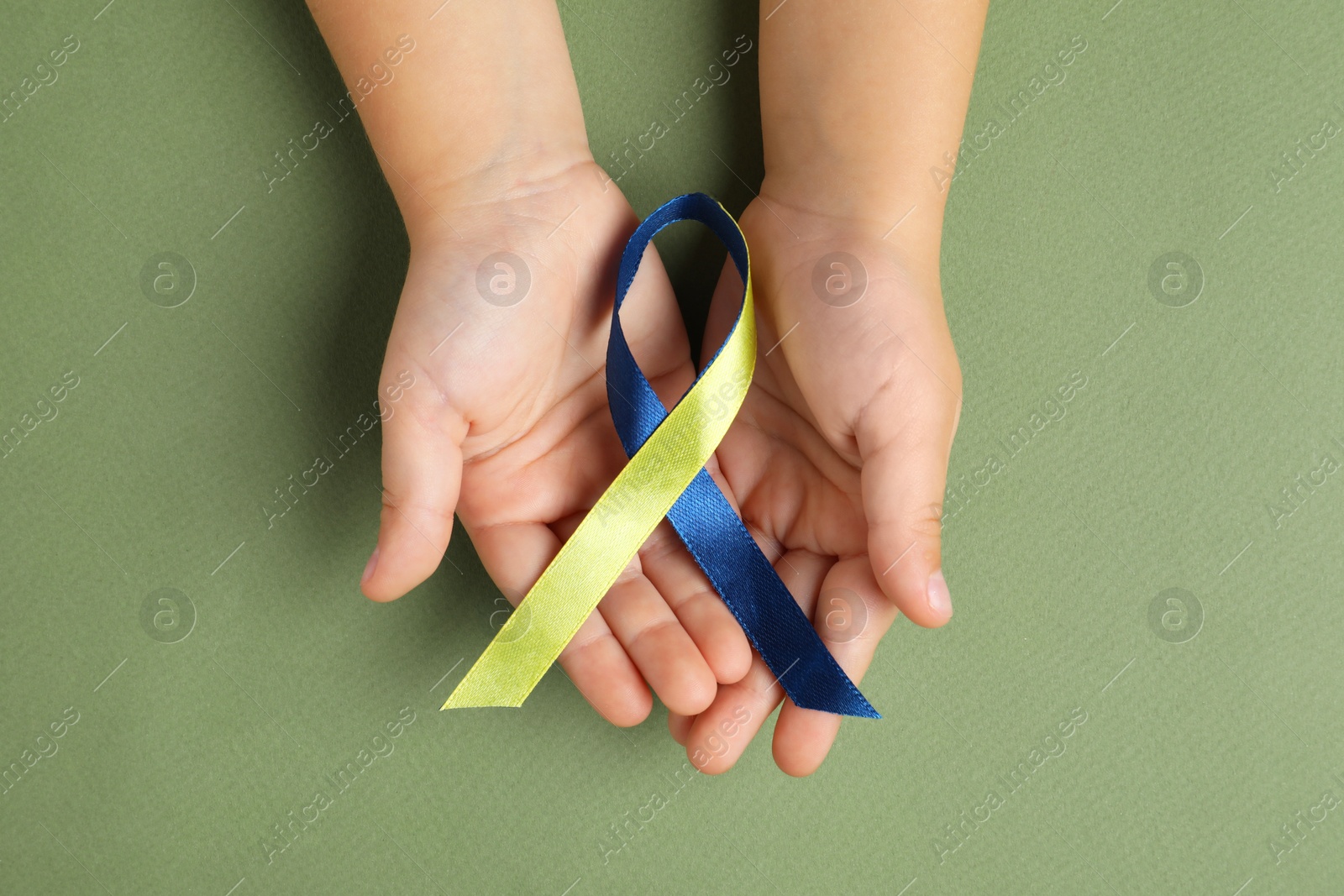 Photo of Child with yellow and blue ribbon on green background, top view. Down syndrome awareness