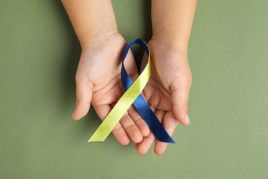 Photo of Child with yellow and blue ribbon on green background, top view. Down syndrome awareness