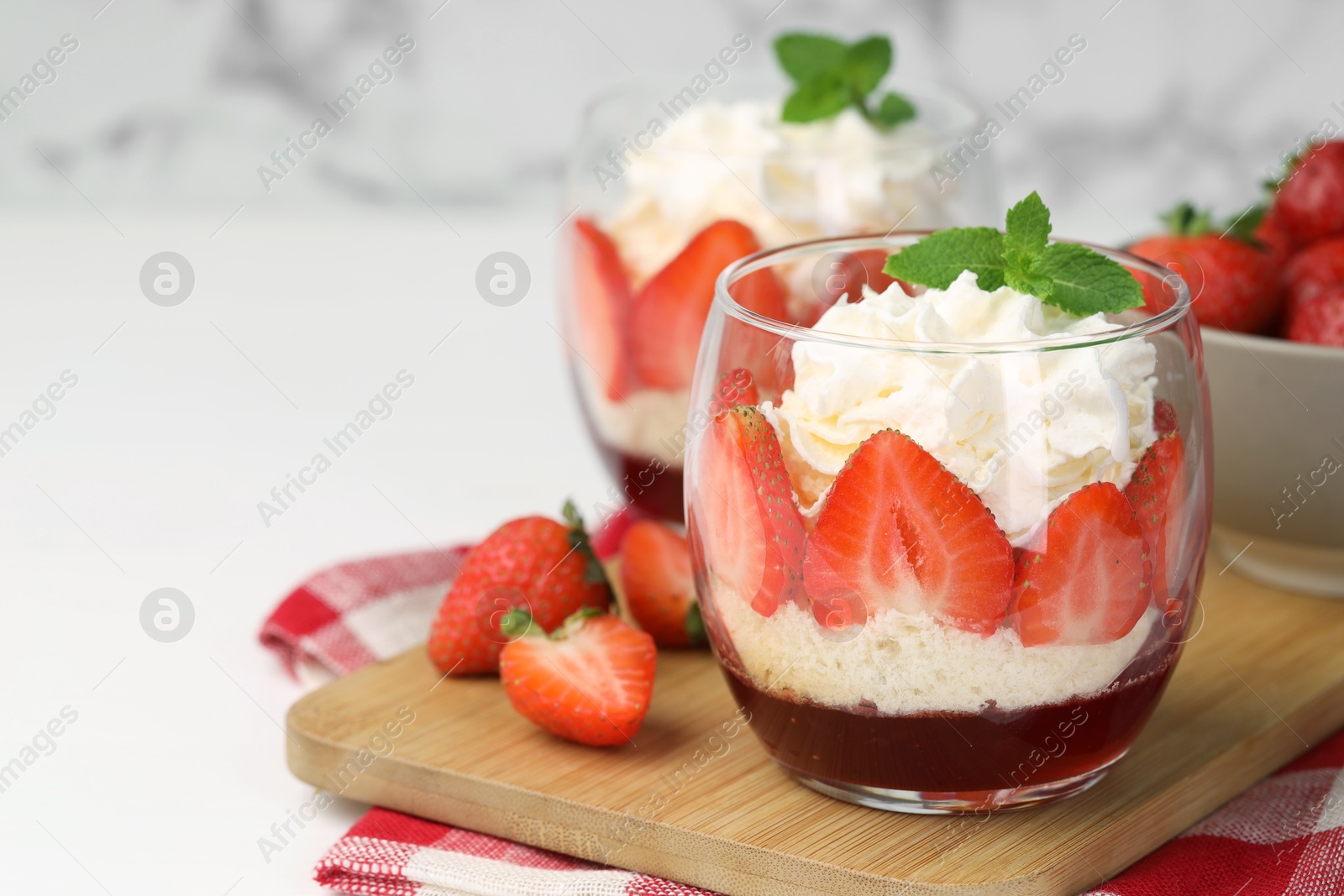 Photo of Tasty trifle dessert. Sponge cake, strawberries, jam and whipped cream in glasses on white table, closeup