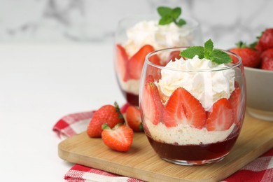 Photo of Tasty trifle dessert. Sponge cake, strawberries, jam and whipped cream in glasses on white table, closeup