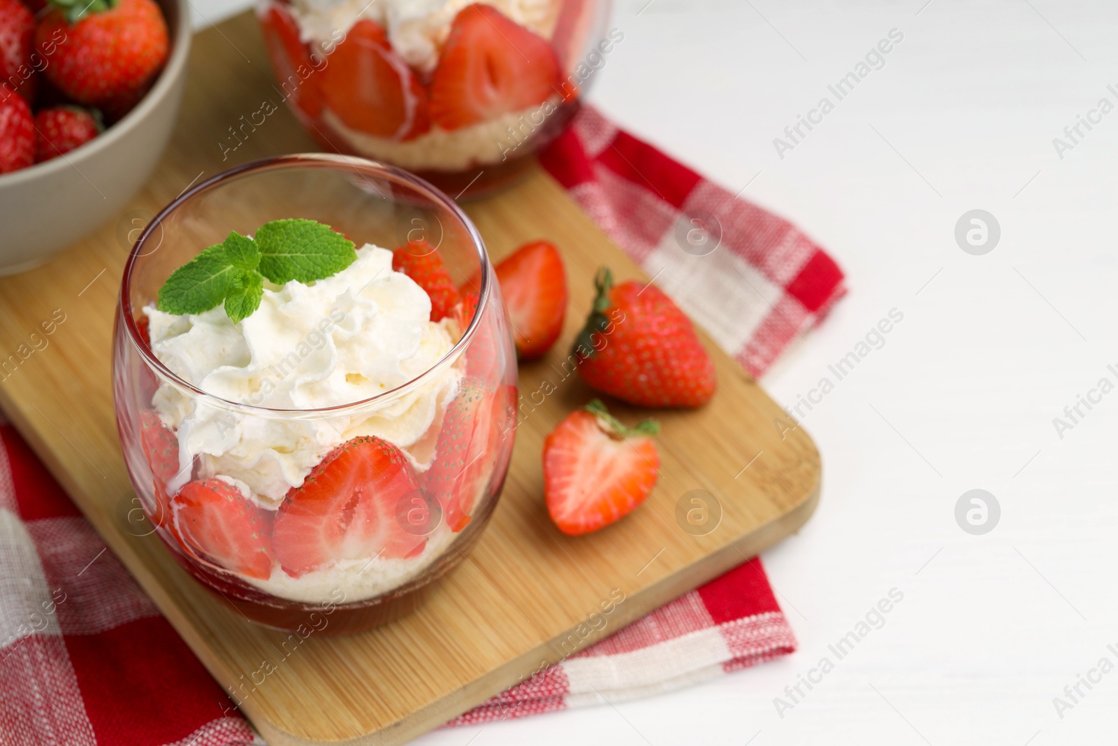 Photo of Tasty trifle dessert. Sponge cake, strawberries, jam and whipped cream in glass on white table, closeup