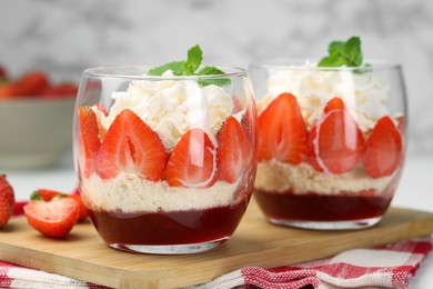 Photo of Tasty trifle dessert. Sponge cake, strawberries, jam and whipped cream in glasses on table, closeup