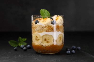 Photo of Tasty trifle dessert. Sponge cake, blueberries, banana and whipped cream in glass on black table