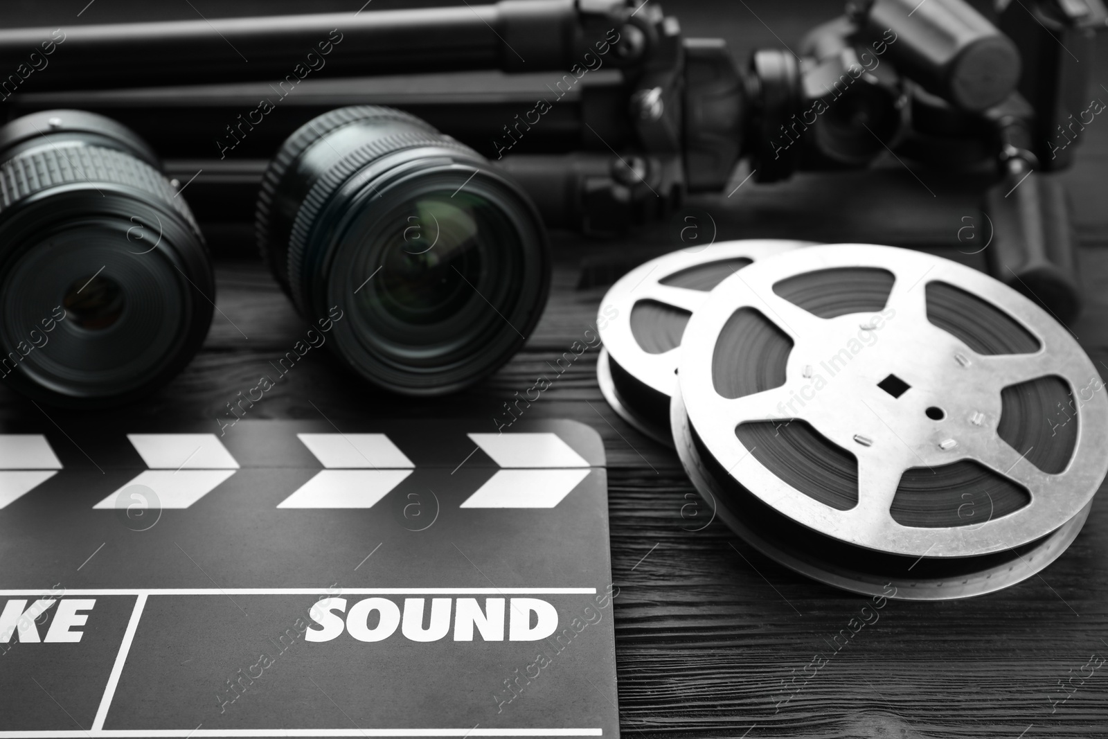 Photo of Movie clapper, camera lens and film reels on black wooden table, closeup