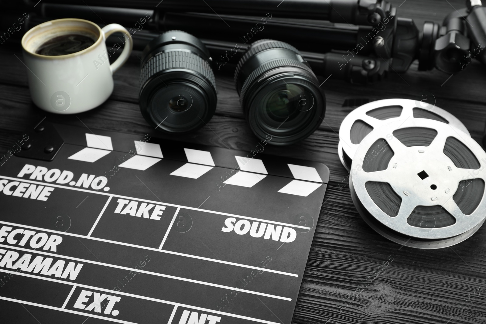 Photo of Movie clapper, camera lens, film reels and cup of coffee on black wooden table, closeup