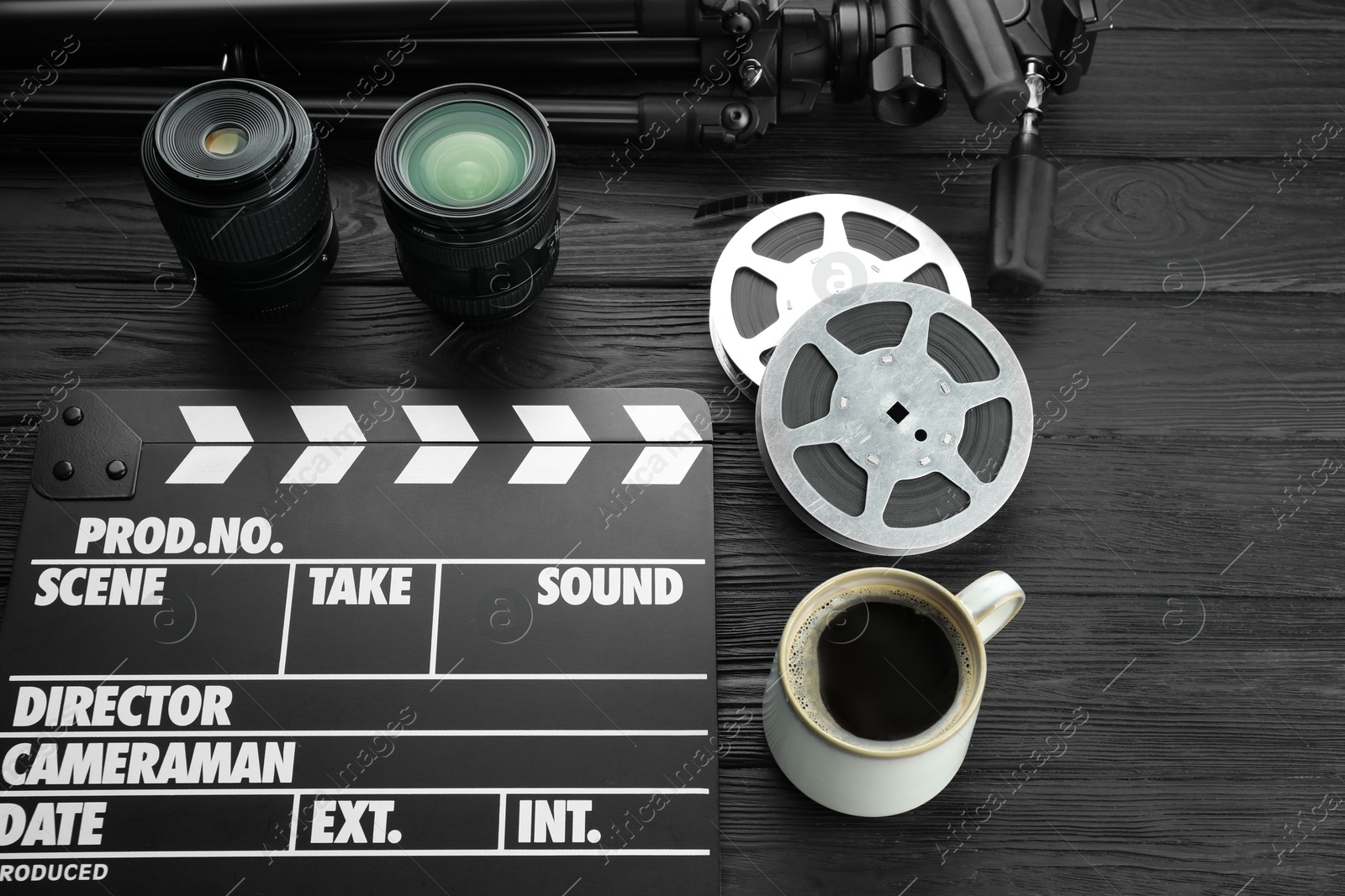 Photo of Movie clapper, camera lens, film reels and cup of coffee on black wooden table, above view