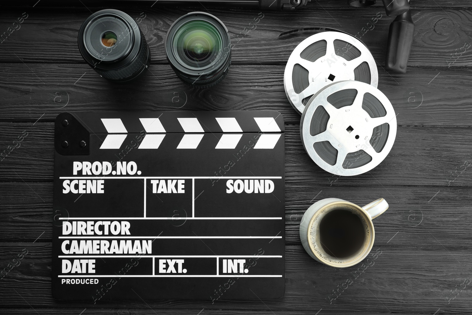 Photo of Movie clapper, camera lens, film reels and cup of coffee on black wooden table, flat lay