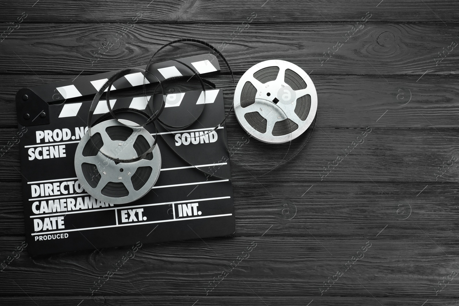 Photo of Movie clapper and film reels on black wooden table, flat lay. Space for text