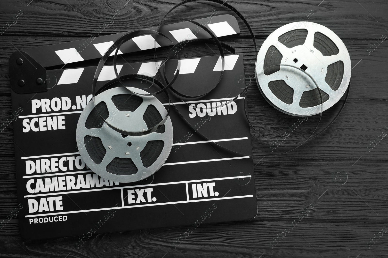 Photo of Movie clapper and film reels on black wooden table, flat lay