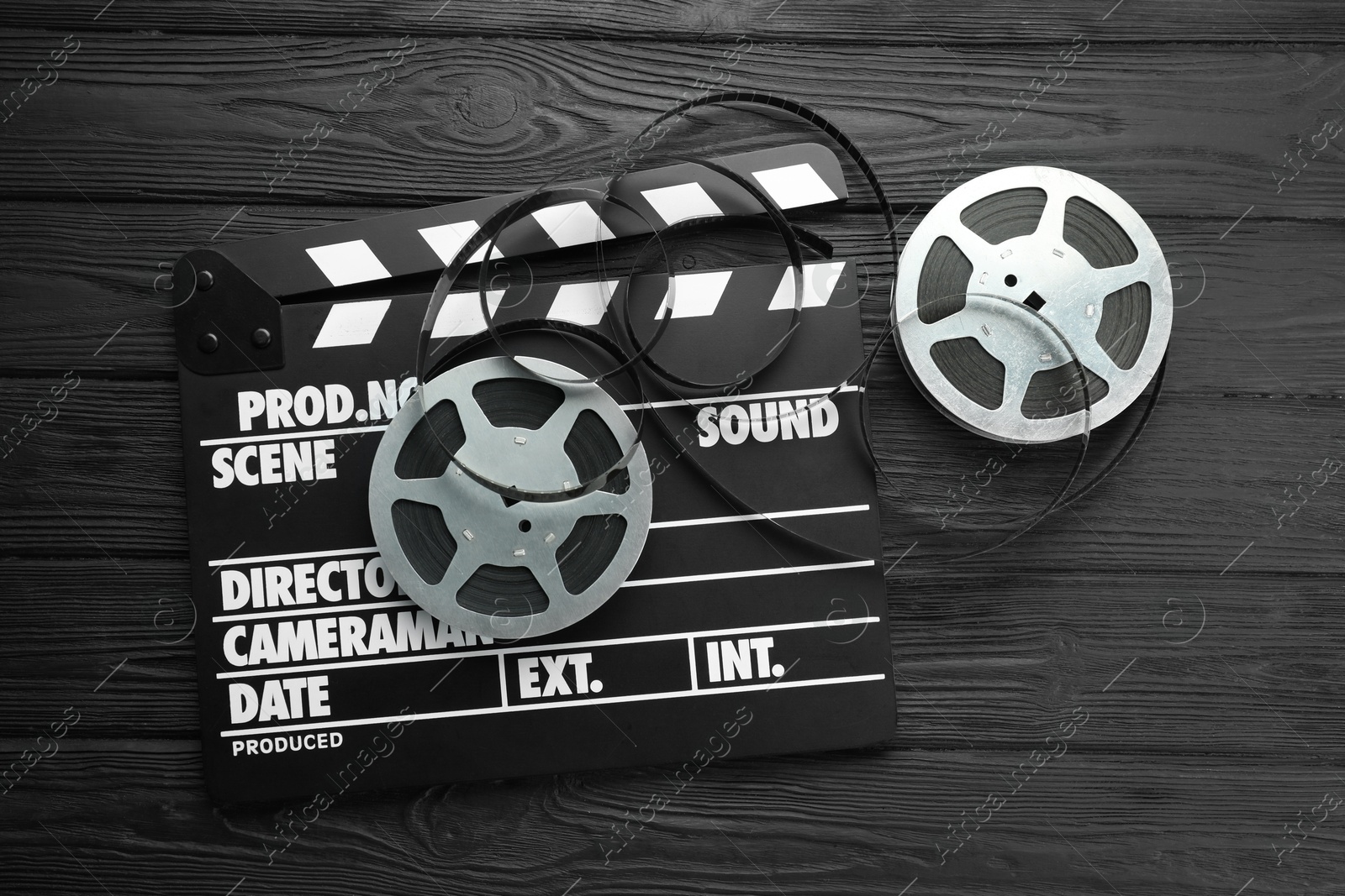 Photo of Movie clapper and film reels on black wooden table, flat lay