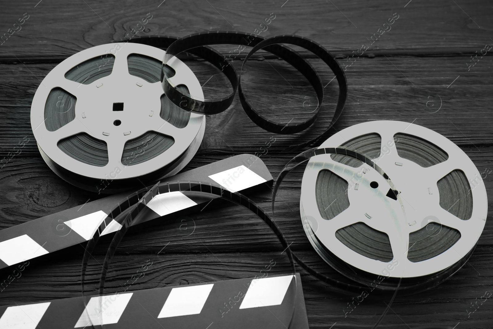 Photo of Movie clapper and film reels on black wooden table, above view