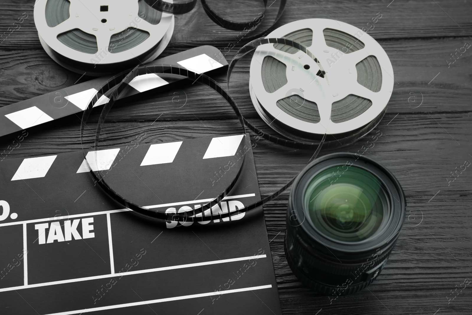 Photo of Movie clapper, film reels and camera lens on black wooden table, above view