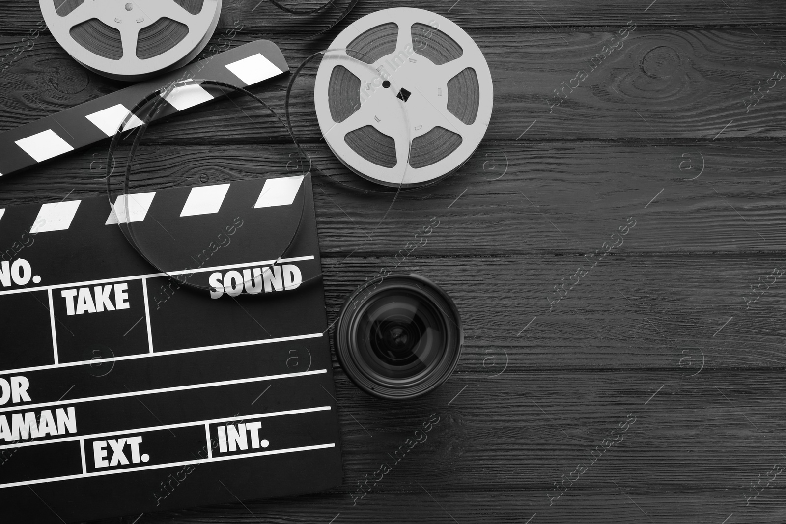 Photo of Movie clapper, film reels and camera lens on black wooden table, flat lay. Space for text