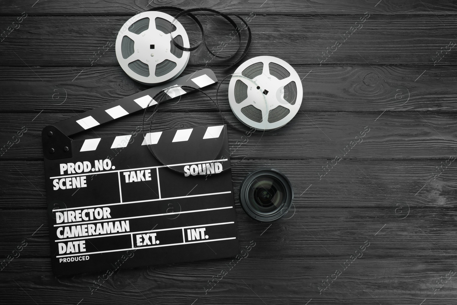 Photo of Movie clapper, film reels and camera lens on black wooden table, flat lay. Space for text