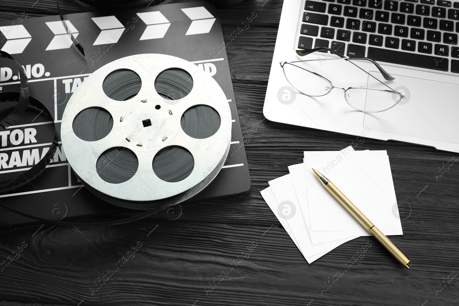 Photo of Movie clapper, film reel and laptop on black wooden table, above view