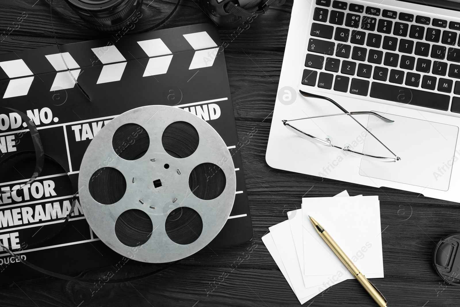 Photo of Movie clapper, film reel and laptop on black wooden table, flat lay