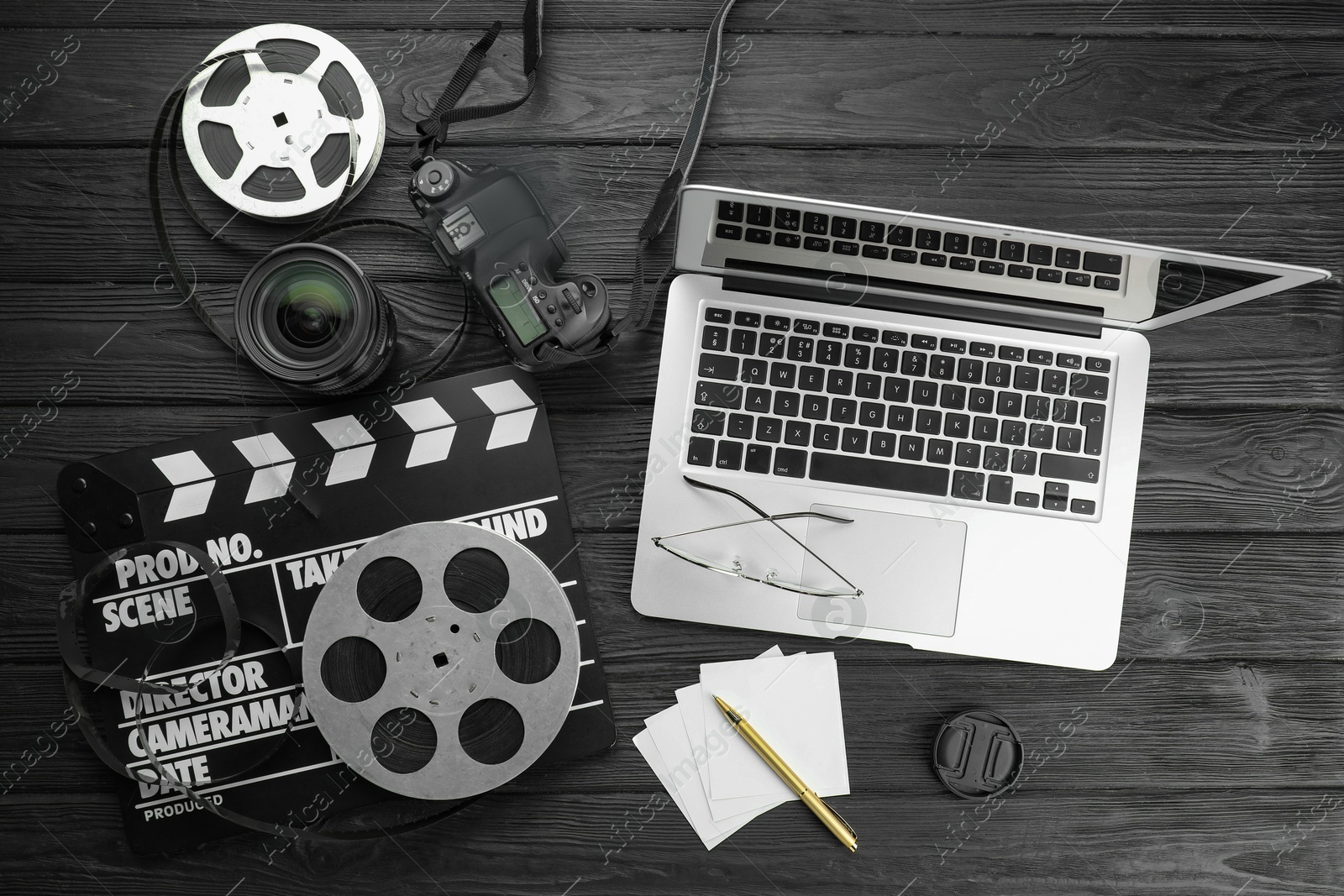 Photo of Movie clapper, film reels, laptop and camera lens on black wooden table, flat lay