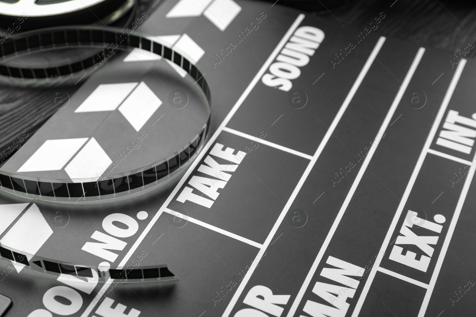 Photo of Movie clapper and film reel on black wooden table, closeup