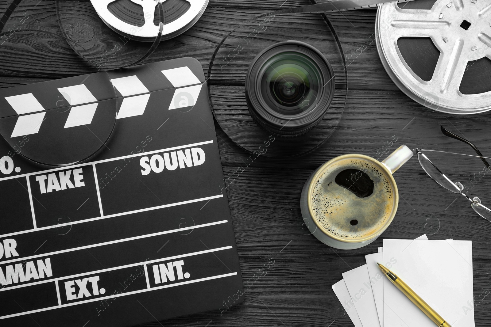 Photo of Movie clapper, film reels and camera lens on black wooden table, flat lay