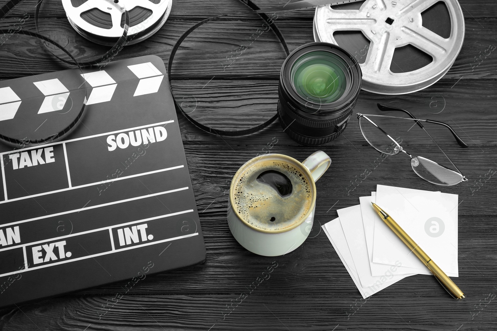 Photo of Movie clapper, film reels and camera lens on black wooden table, above view