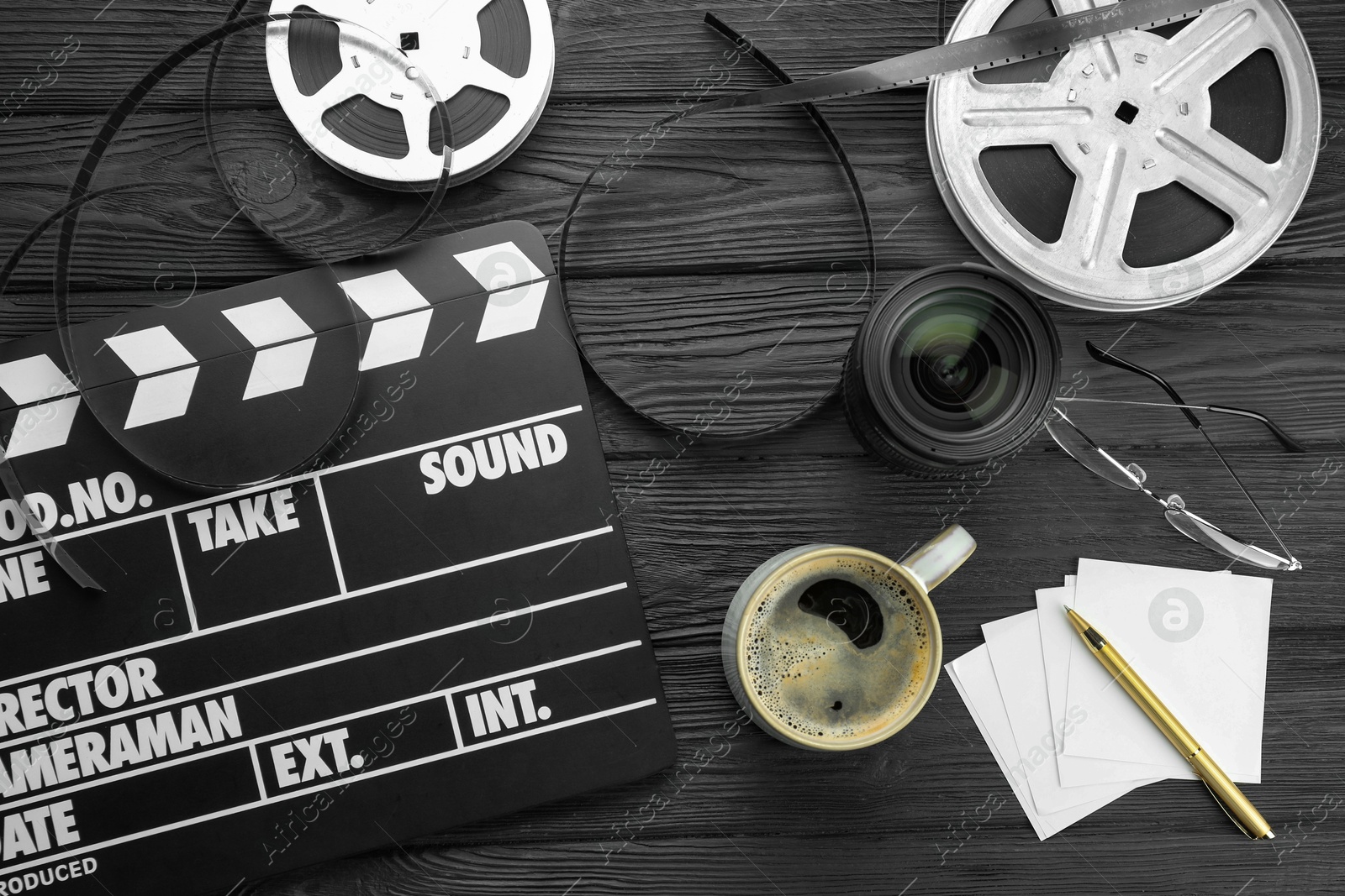 Photo of Movie clapper, film reels and camera lens on black wooden table, flat lay