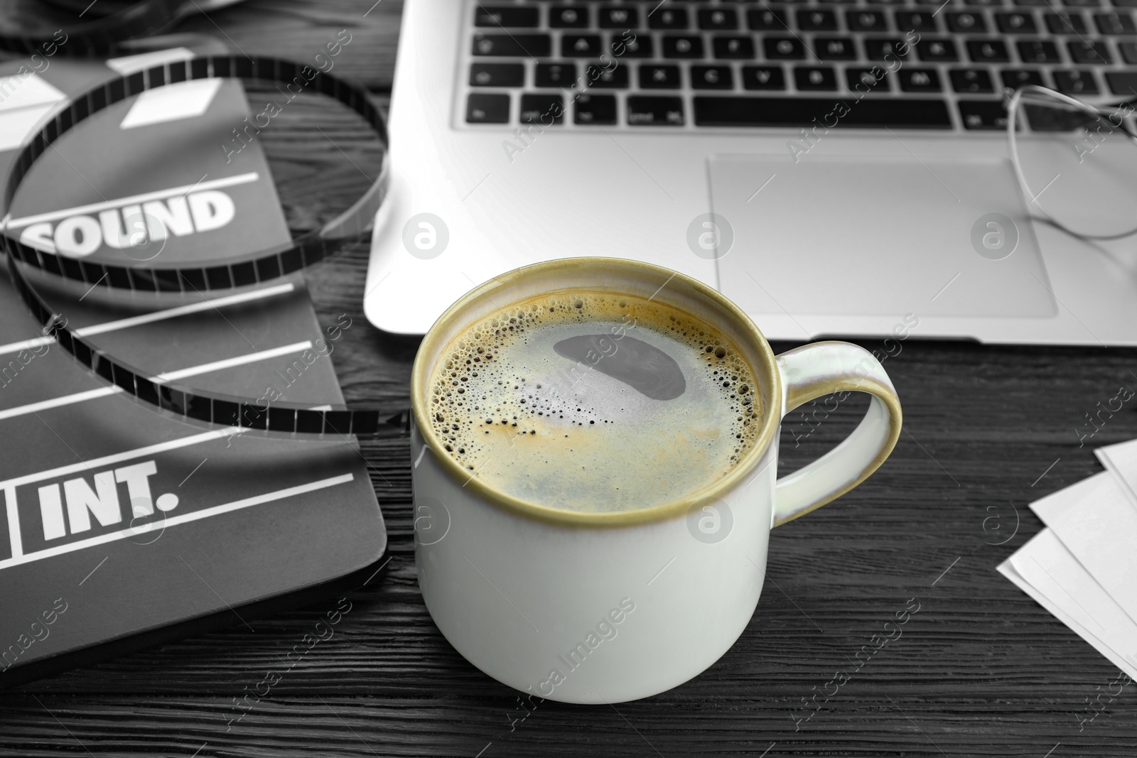 Photo of Movie clapper, film reel and cup of coffee on black wooden table, closeup