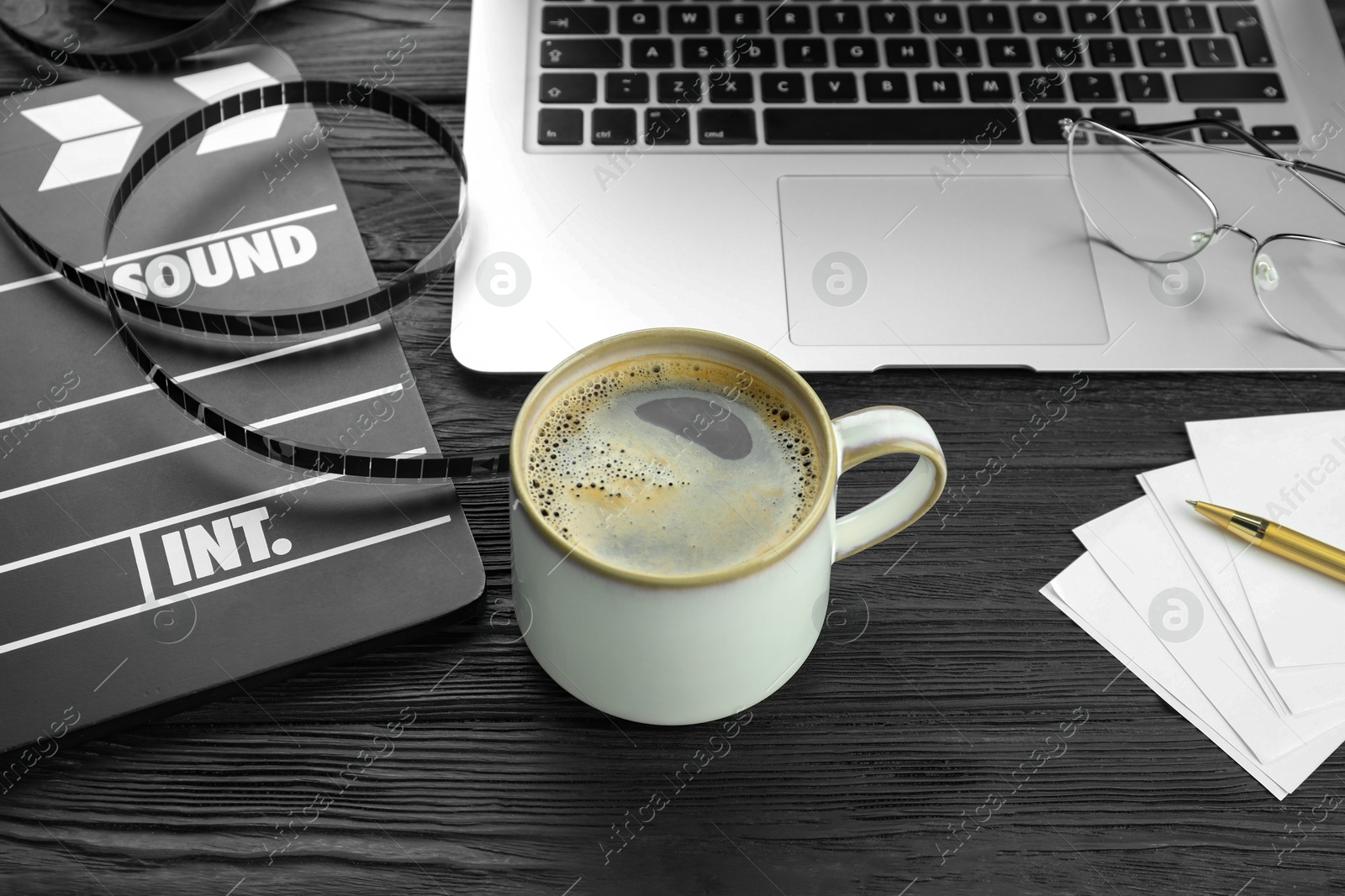 Photo of Movie clapper, film reel and cup of coffee on black wooden table, closeup