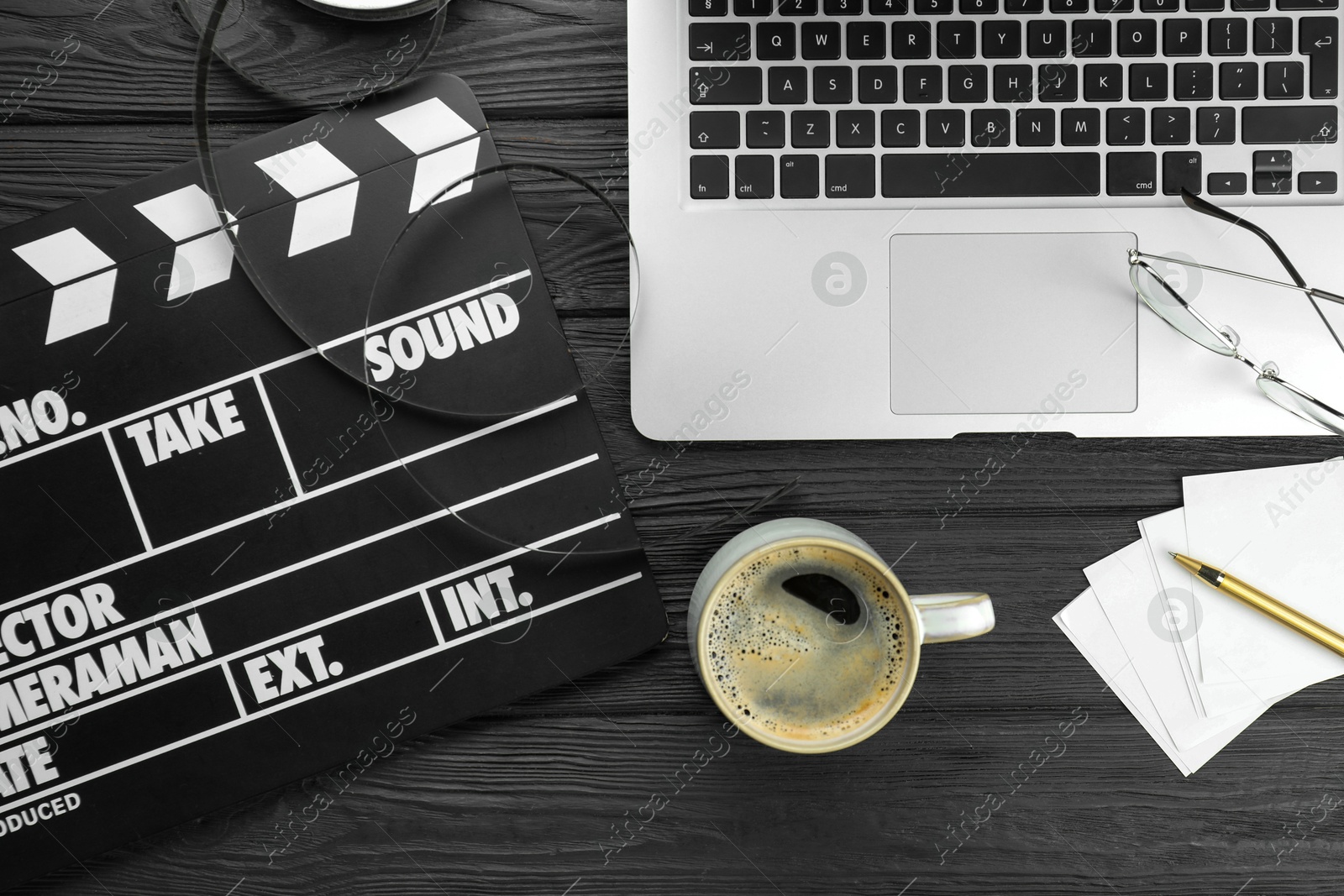 Photo of Movie clapper, film reel, laptop and cup of coffee on black wooden table, flat lay