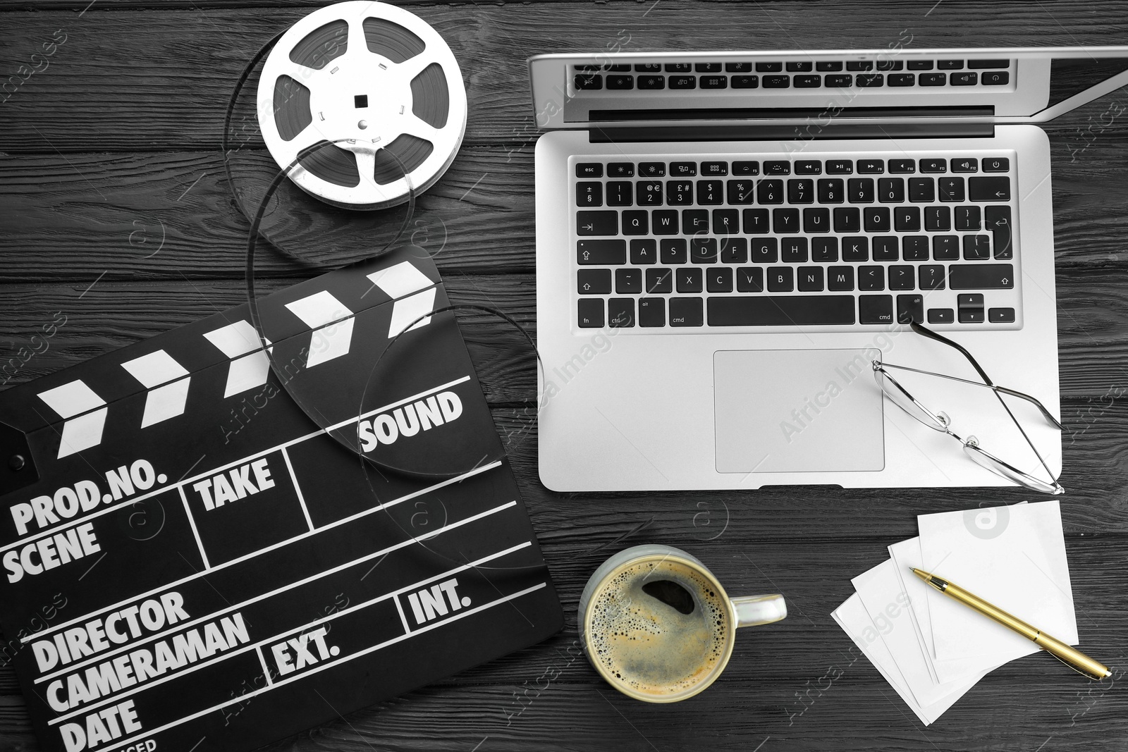 Photo of Movie clapper, film reel, laptop and cup of coffee on black wooden table, flat lay