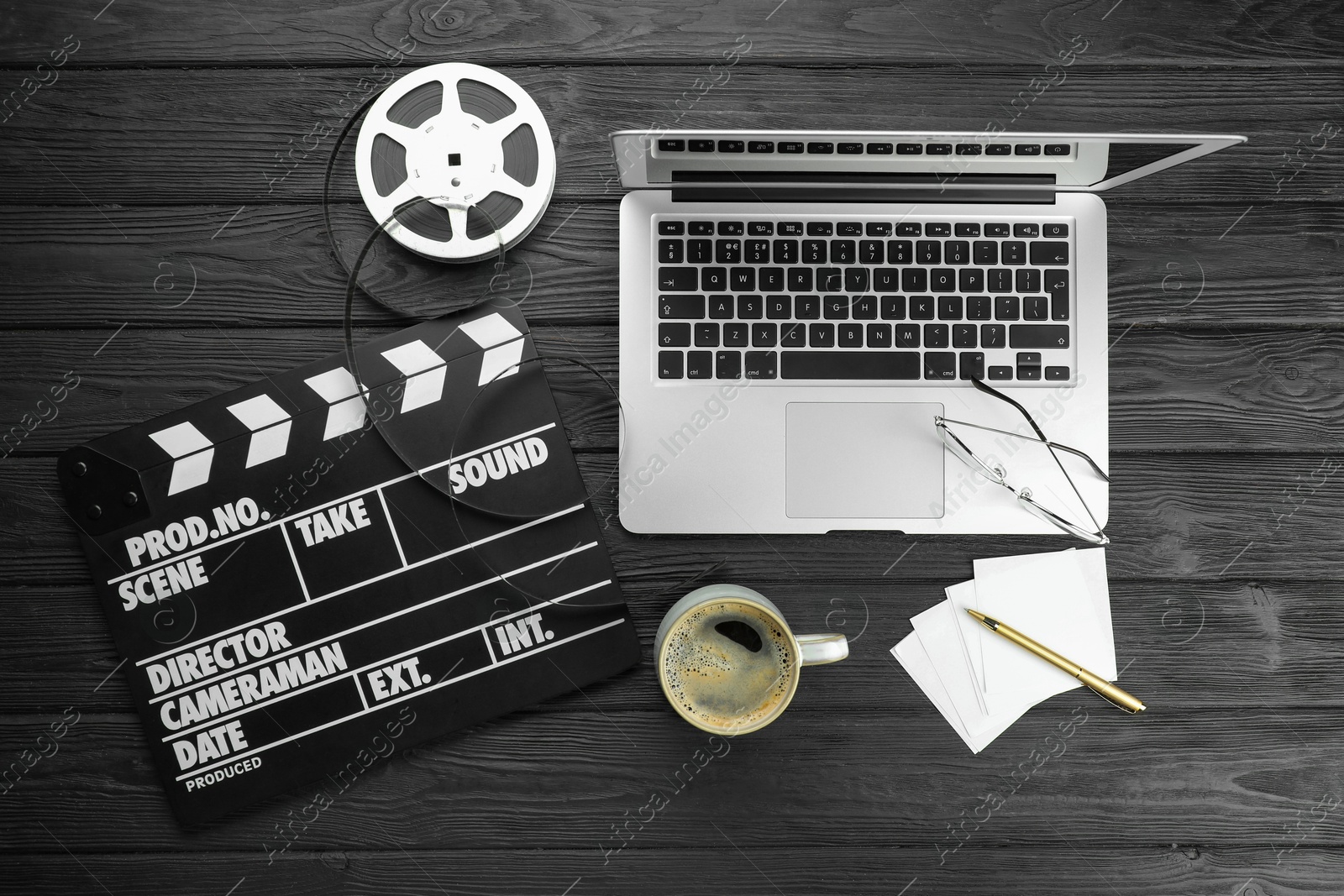 Photo of Movie clapper, film reel, laptop and cup of coffee on black wooden table, flat lay