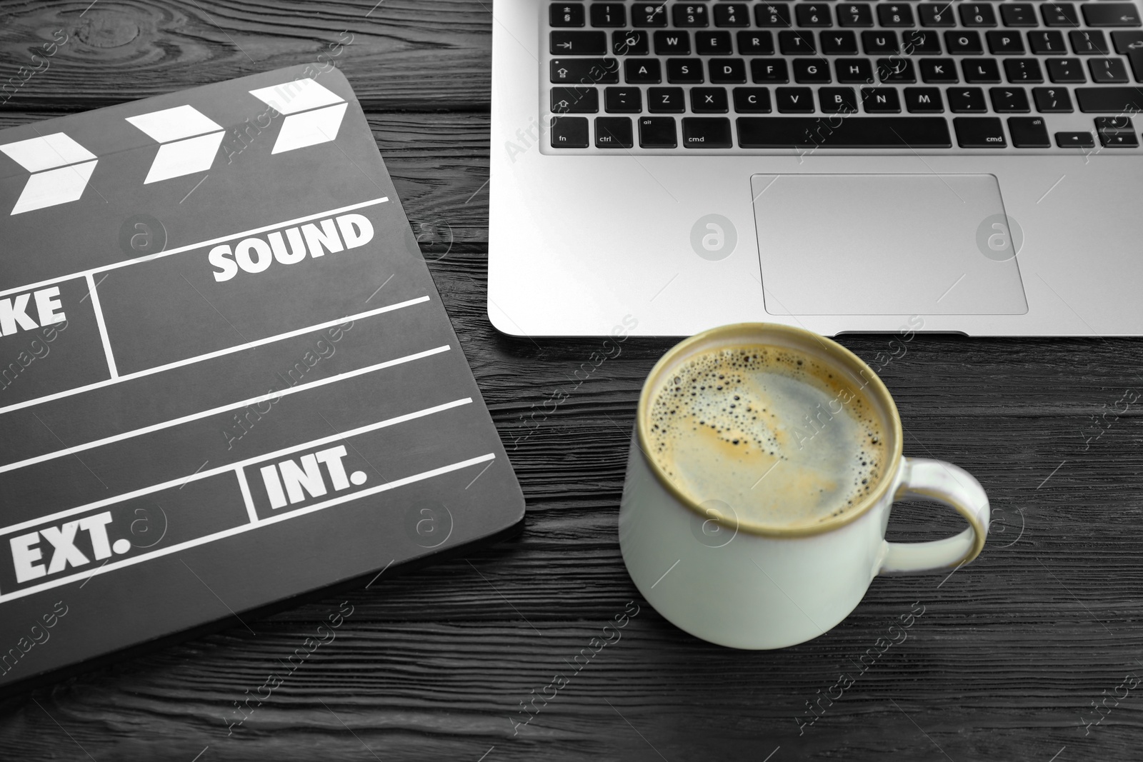 Photo of Movie clapper, laptop and cup of coffee on black wooden table, closeup