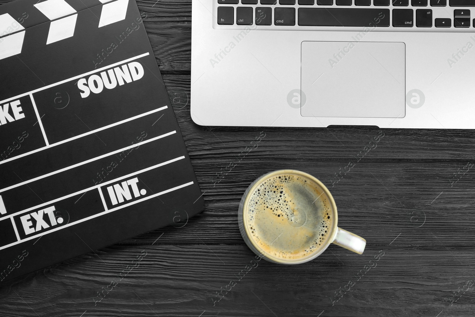 Photo of Movie clapper, laptop and cup of coffee on black wooden table, flat lay