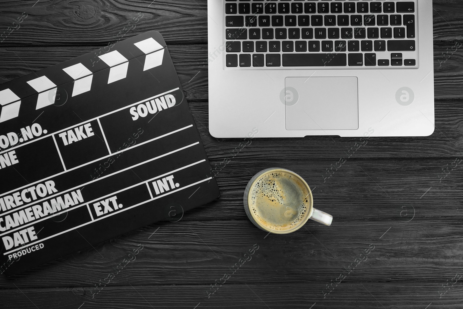 Photo of Movie clapper, laptop and cup of coffee on black wooden table, flat lay