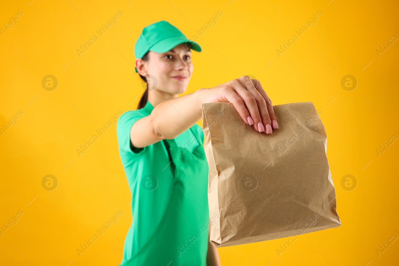 Photo of Fast-food worker with paper bag on orange background, selective focus