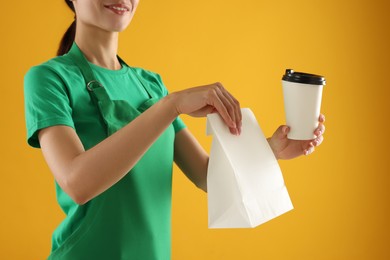 Photo of Fast-food worker with paper bag and cup on orange background, closeup