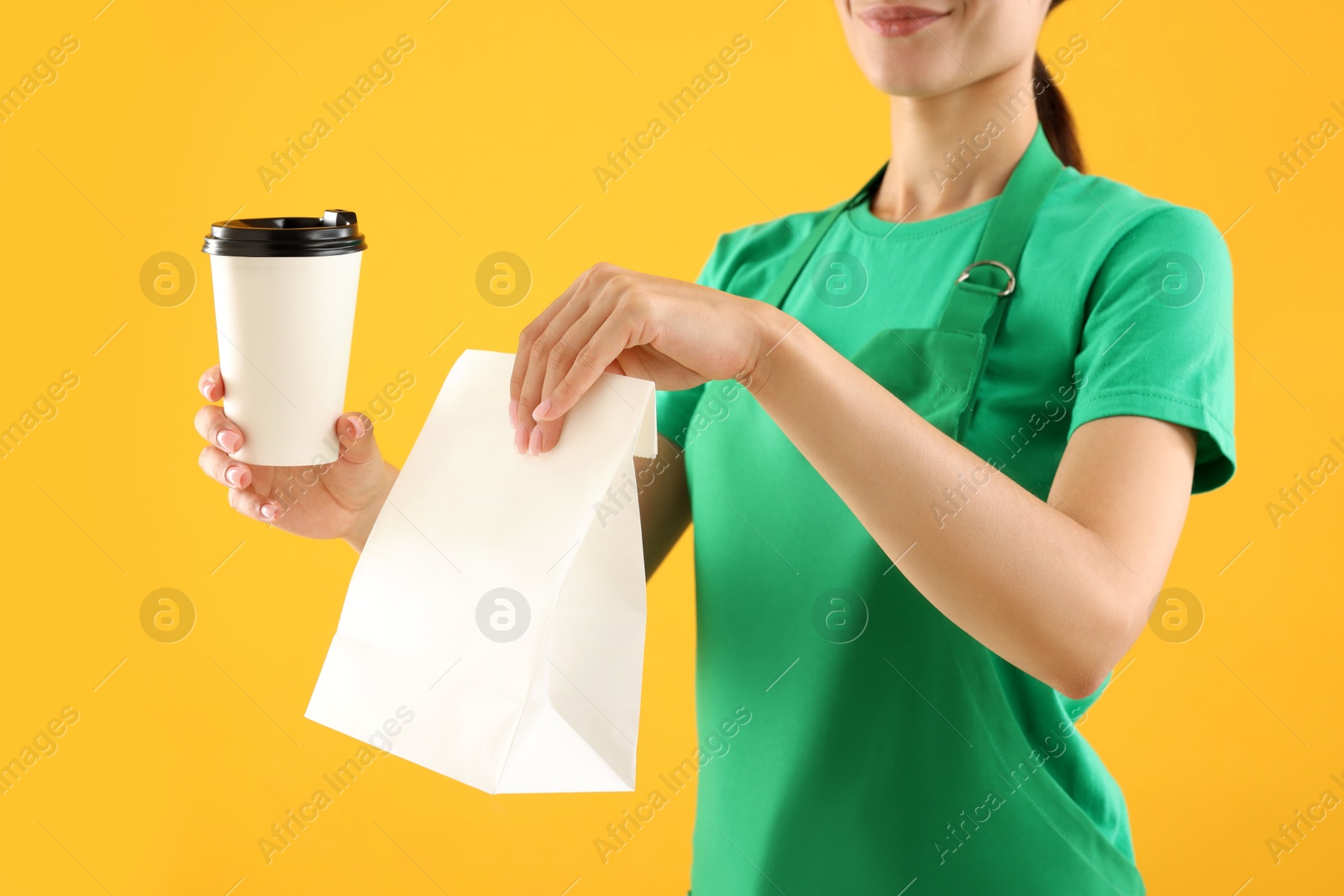 Photo of Fast-food worker with paper bag and cup on orange background, closeup