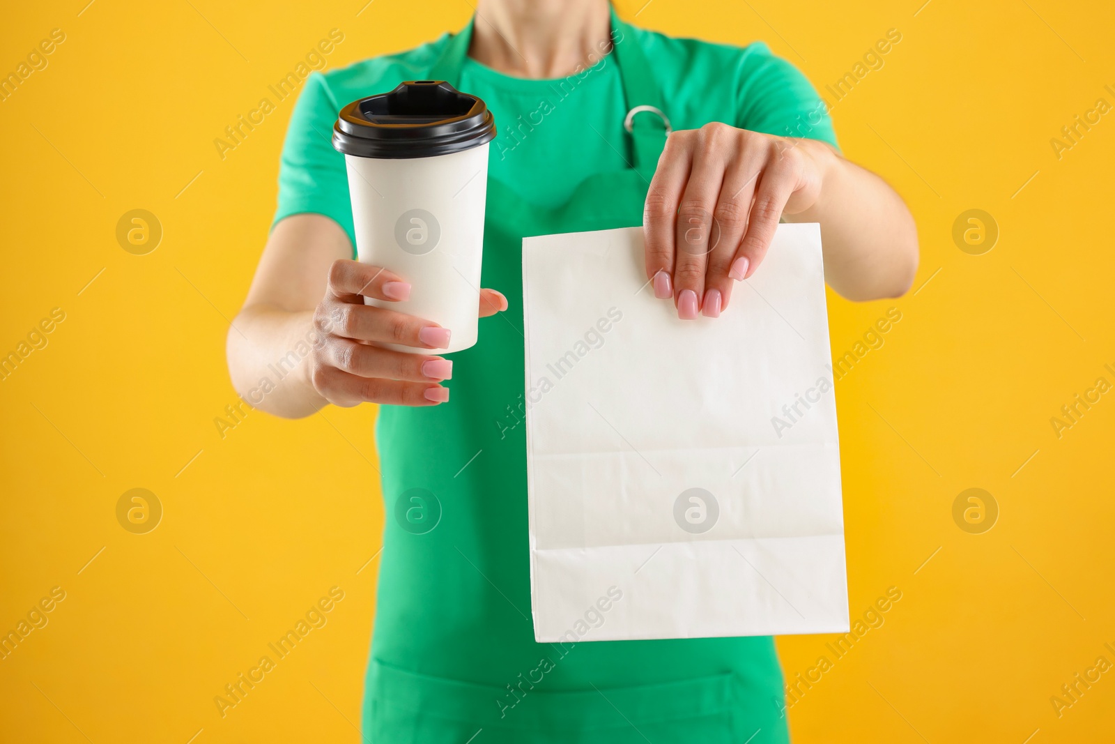 Photo of Fast-food worker with paper bag and cup on orange background, closeup