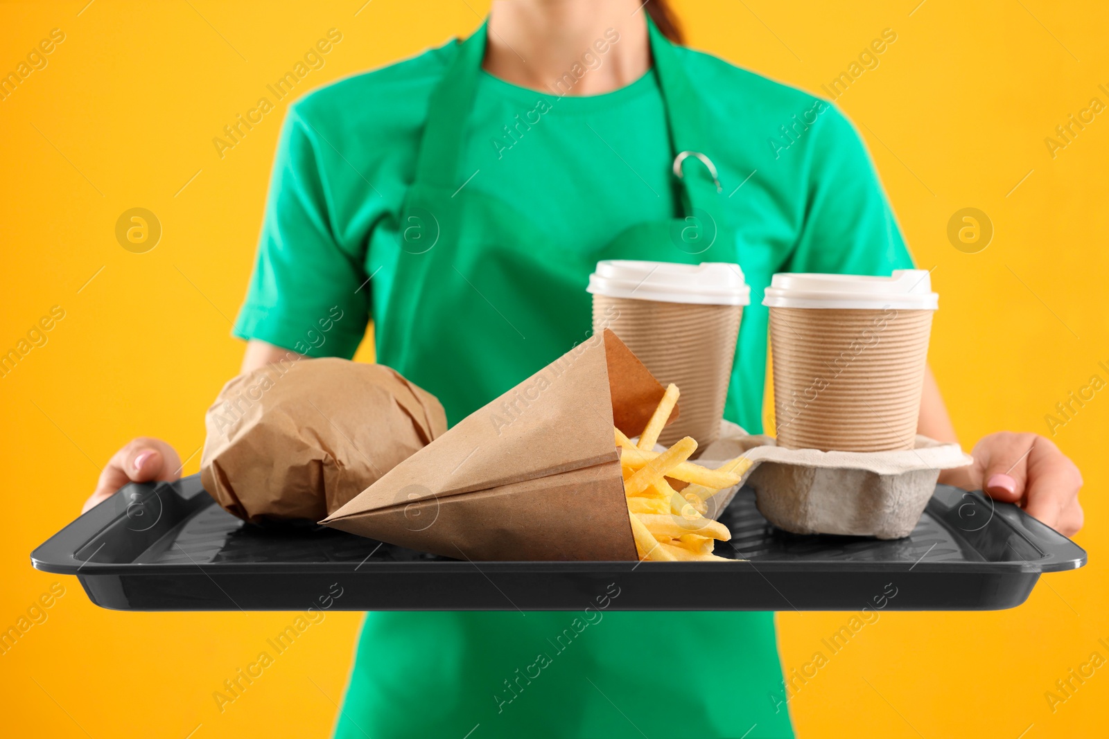 Photo of Fast-food worker holding tray with order on orange background, closeup