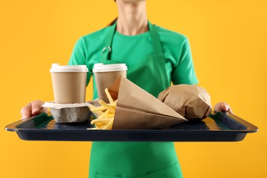 Photo of Fast-food worker holding tray with order on orange background, closeup