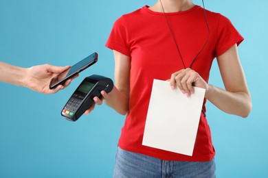 Photo of Fast-food worker taking payment from client via terminal on light blue background, closeup