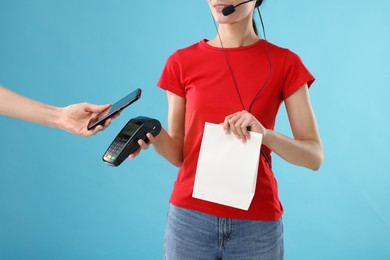 Photo of Fast-food worker taking payment from client via terminal on light blue background, closeup