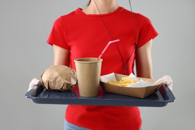 Fast-food worker holding tray with order on gray background, closeup