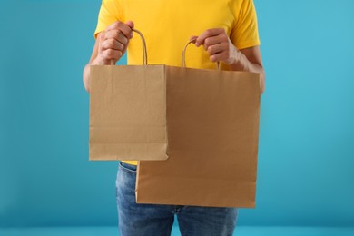 Photo of Fast-food worker with paper bags on light blue background, closeup