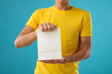 Photo of Fast-food worker with paper bag on light blue background, closeup