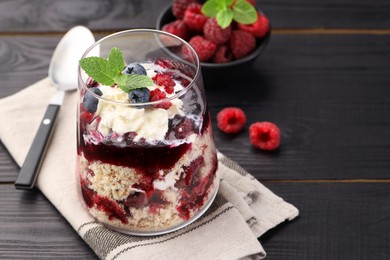 Photo of Tasty trifle dessert. Berries, sponge cake and whipped cream in glass on black wooden table, space for text