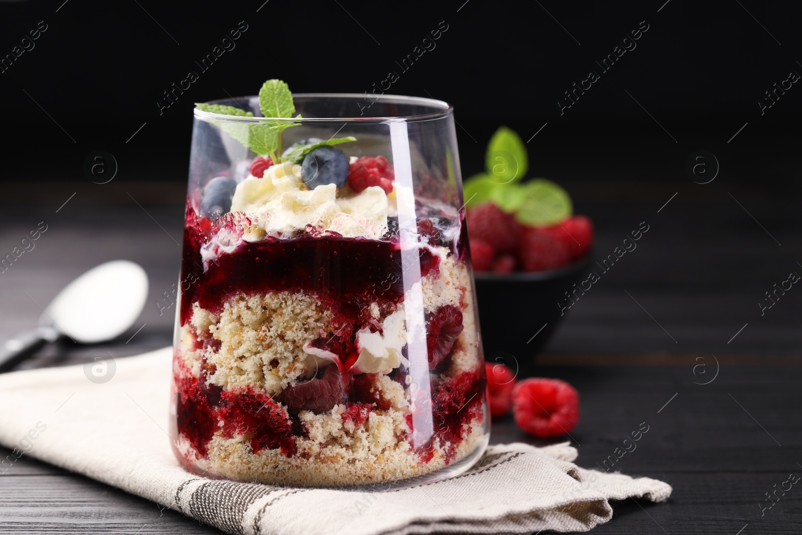 Photo of Tasty trifle dessert. Berries, sponge cake and whipped cream in glass on black wooden table